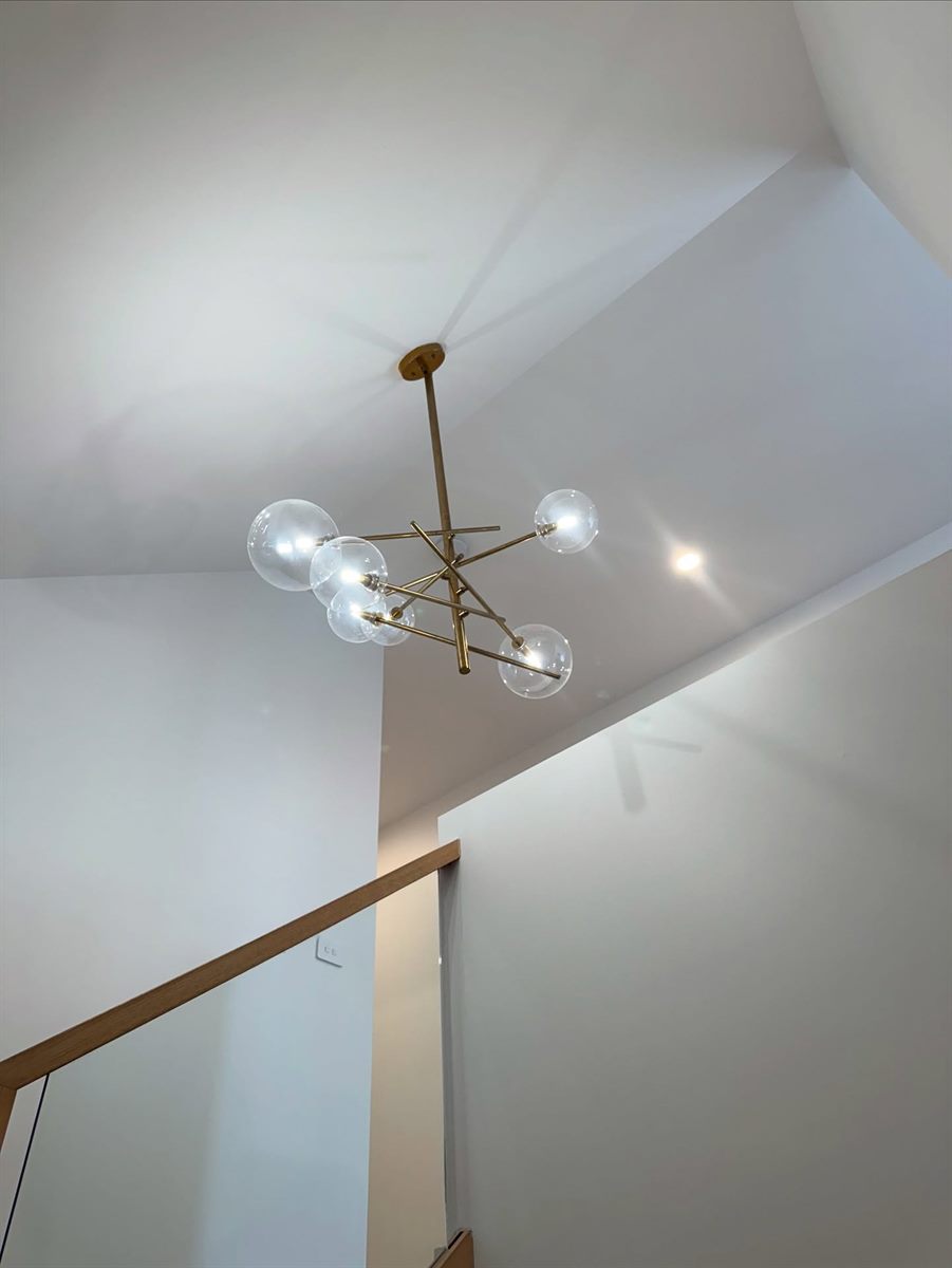 Looking up a stairwell to a brass pendant against angled white ceiling planes.