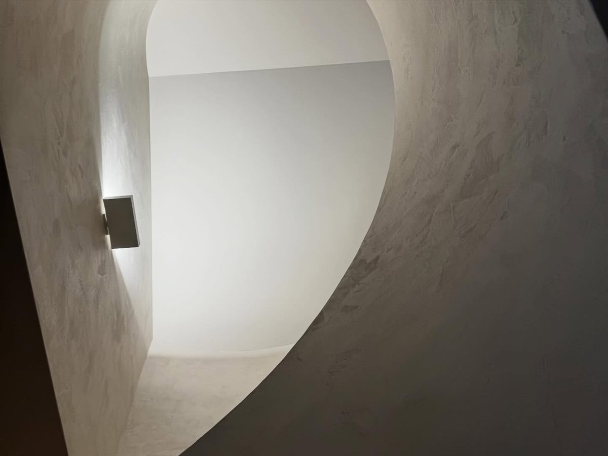 A curved plastered wall and soffit lit by a single wall light.