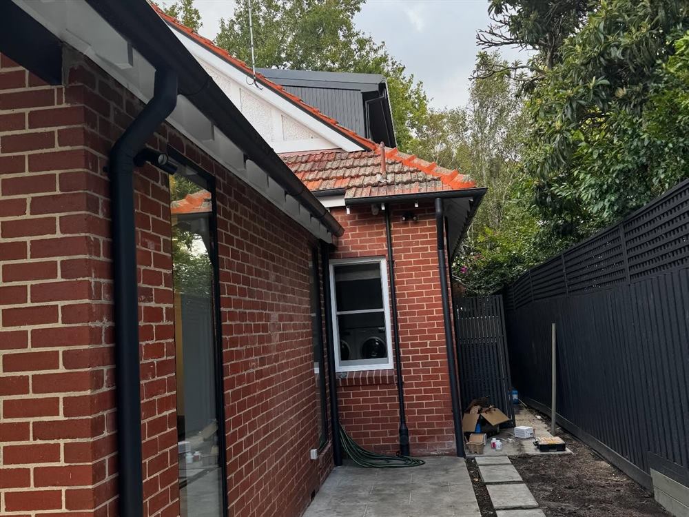 Red brick side elevation with a black boundary fence, tiled roof and a paved path.