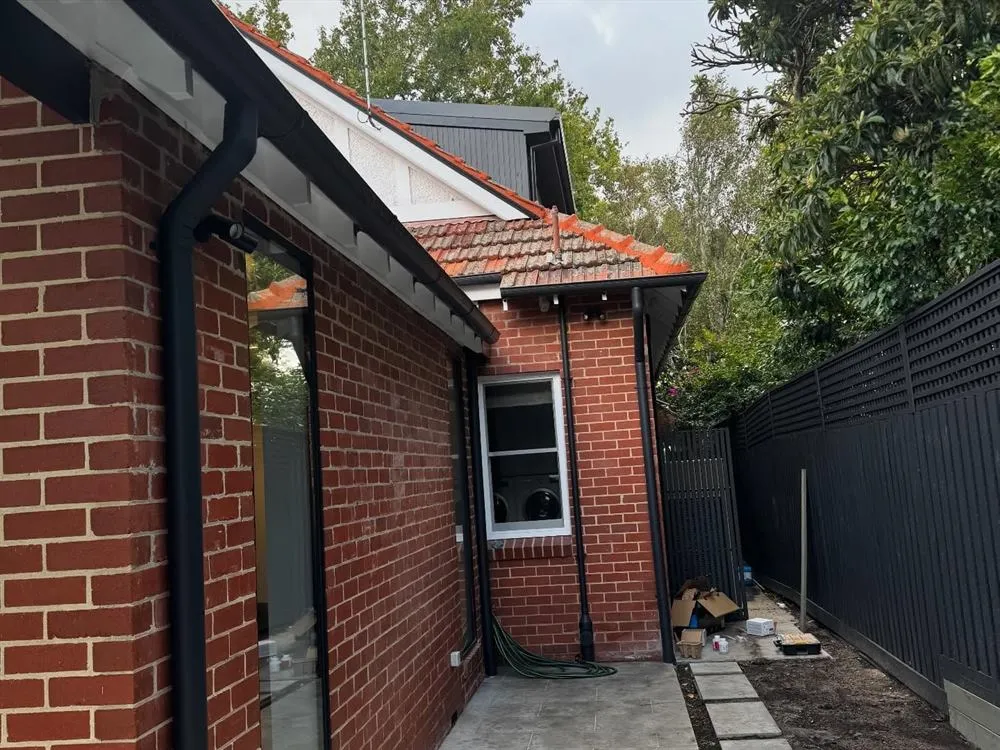 Red brick side elevation with a black boundary fence, tiled roof and a paved path.