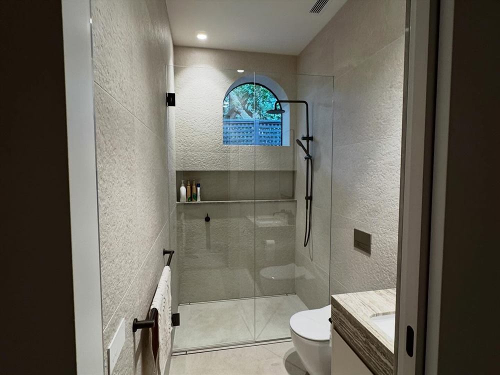 Bathroom with a walk-in shower and an arched leadlight window in stone tiling.
