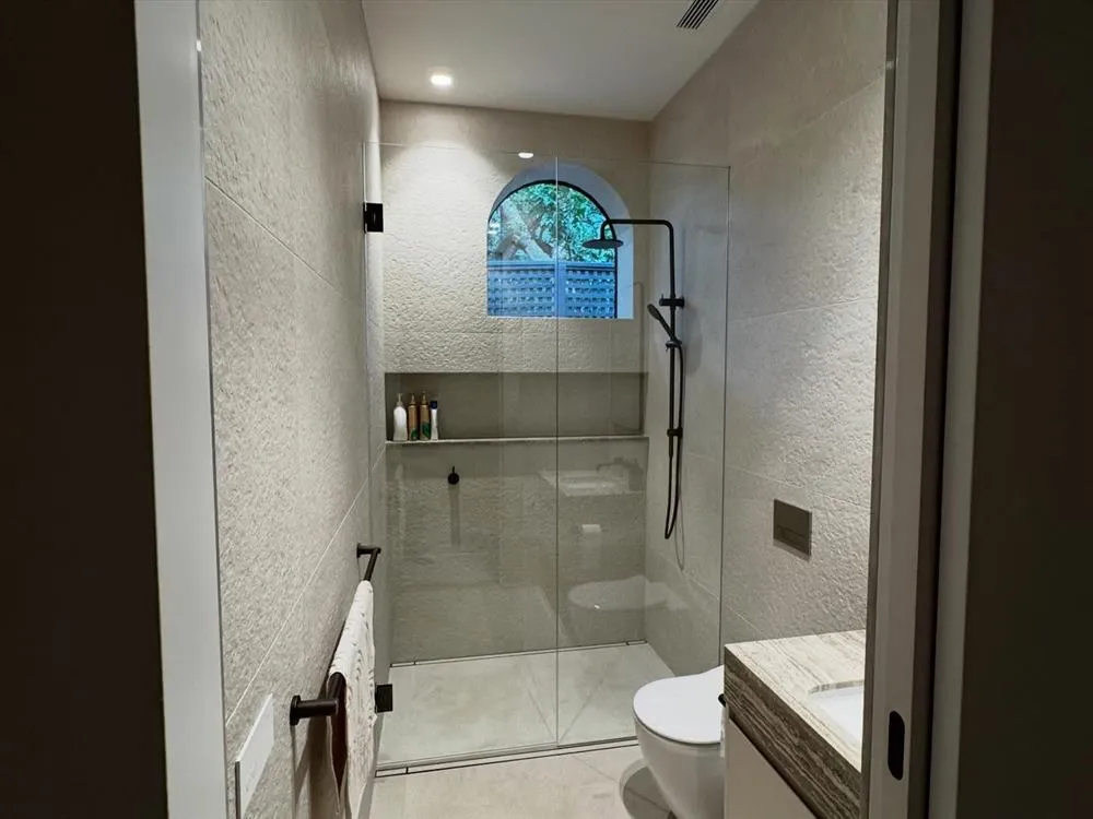 Bathroom with a walk-in shower and an arched leadlight window in stone tiling.
