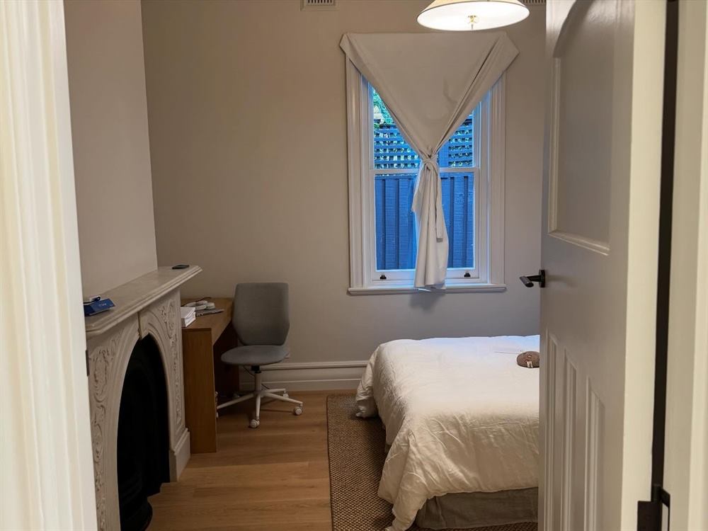 Bedroom with an original fireplace, a leadlight window, a desk and timber floors.