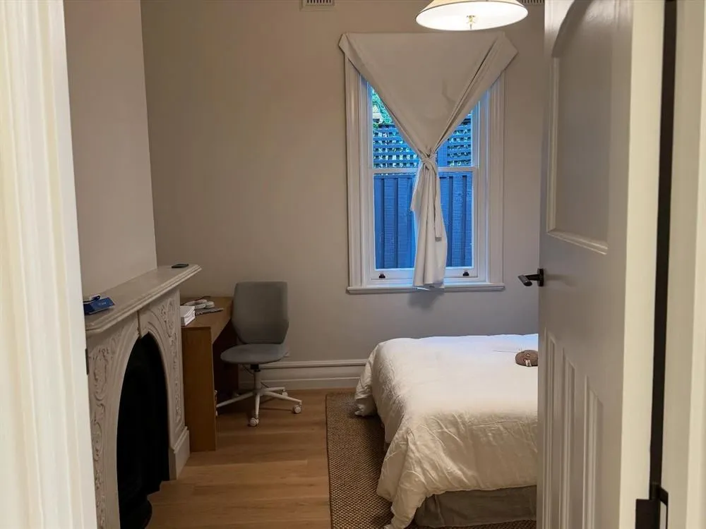 Bedroom with an original fireplace, a leadlight window, a desk and timber floors.