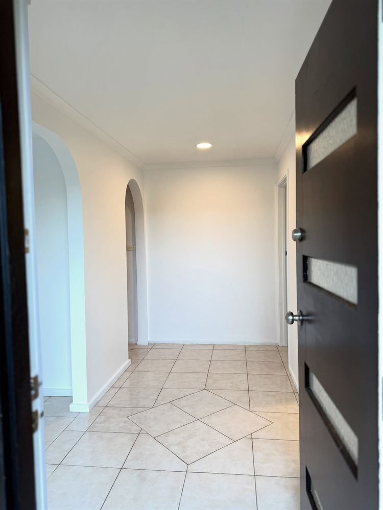 Entry hall with an arched opening, dark timber front door with frosted glazing and a patterned tiled floor.
