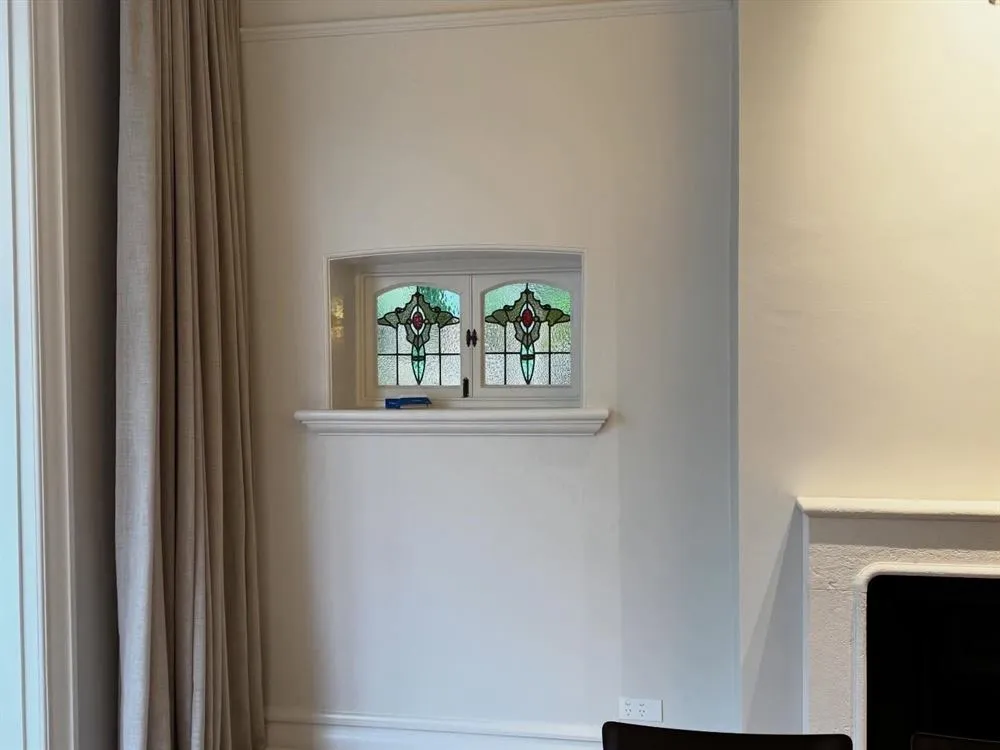 A leadlight window set into a white wall beside a curtain and mantel.