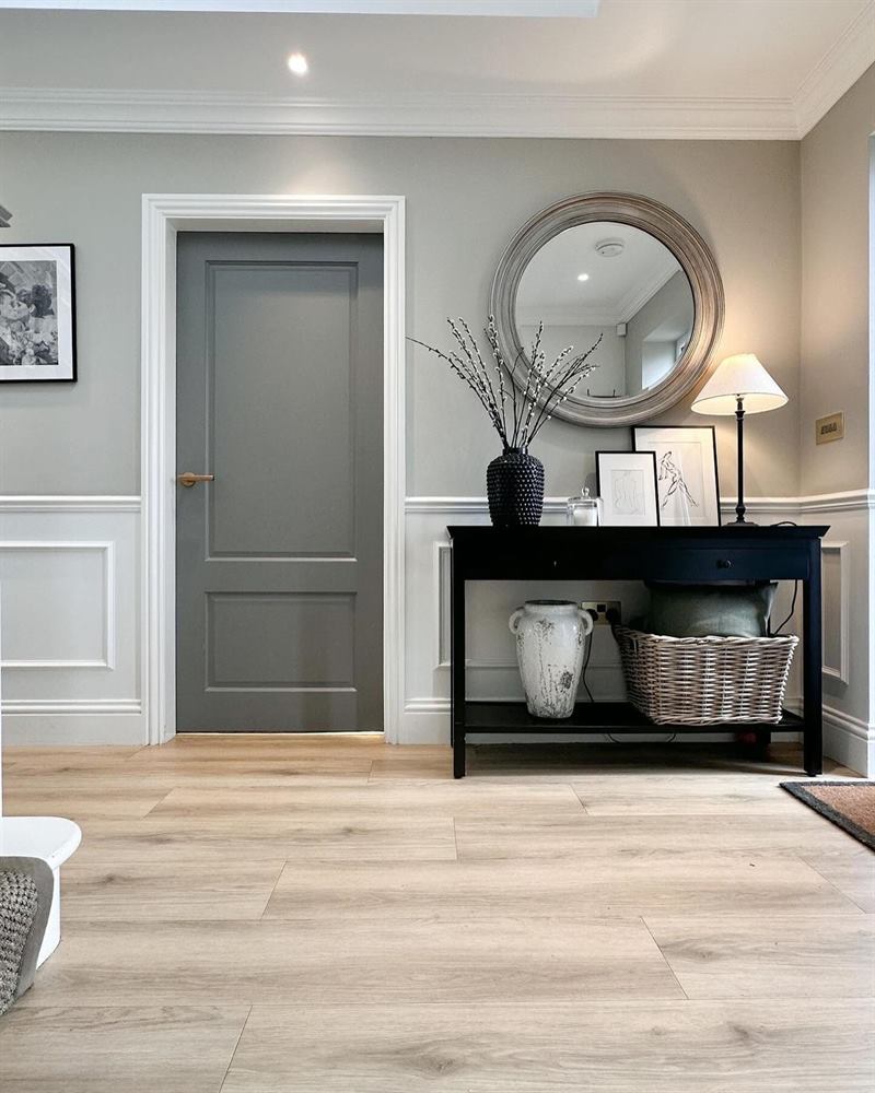 Entry with a grey panelled door, wall panelling, a round mirror and a black console table.