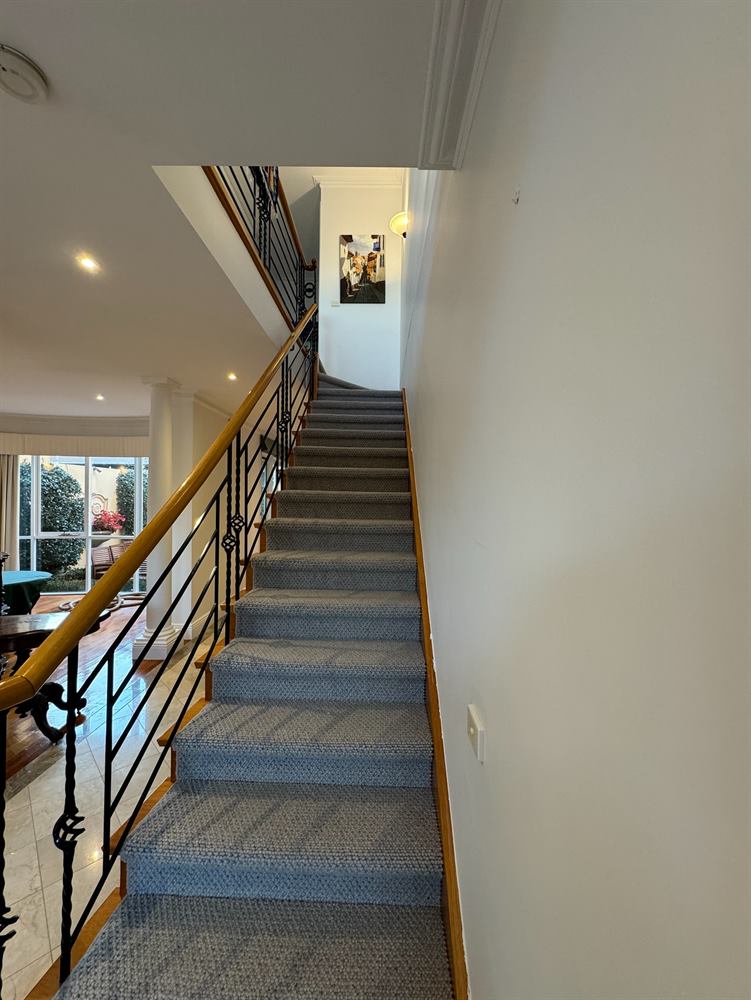 Staircase with a timber handrail, black metal balustrade, patterned carpet runner and framed pictures.