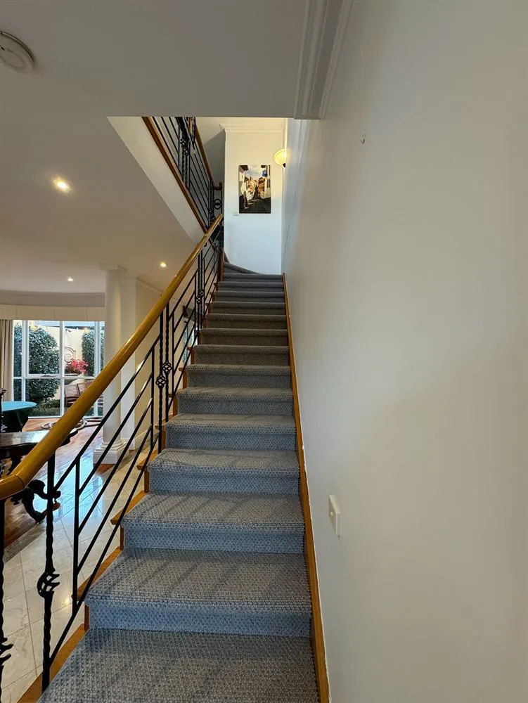 Staircase with a timber handrail, black metal balustrade, patterned carpet runner and framed pictures.