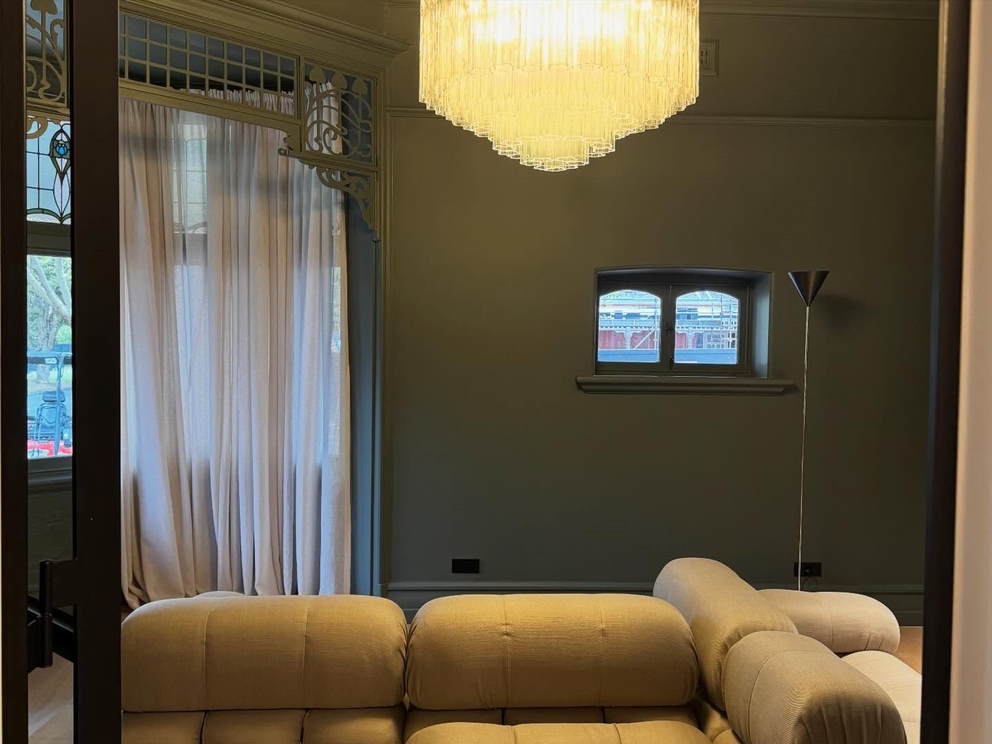 Sitting room in a deep olive with a tiered amber chandelier, leadlight window and full-length curtains.