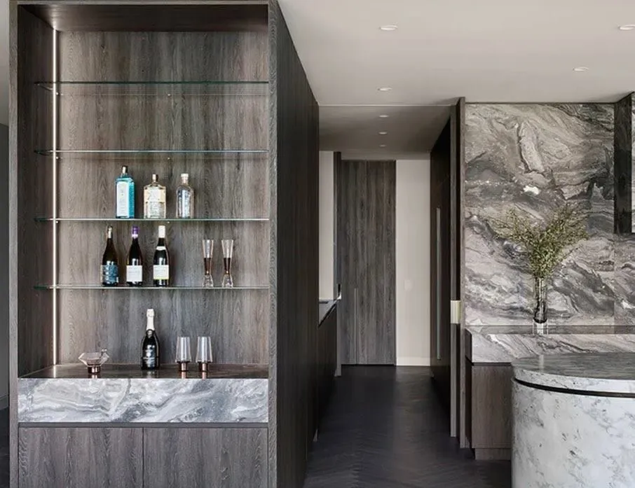Bar with bottles on backlit shelving, marble surfaces and dark joinery.
