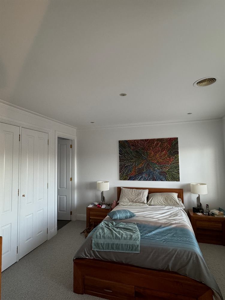 Bedroom with a timber bed, framed artwork and built-in robes against cream walls.