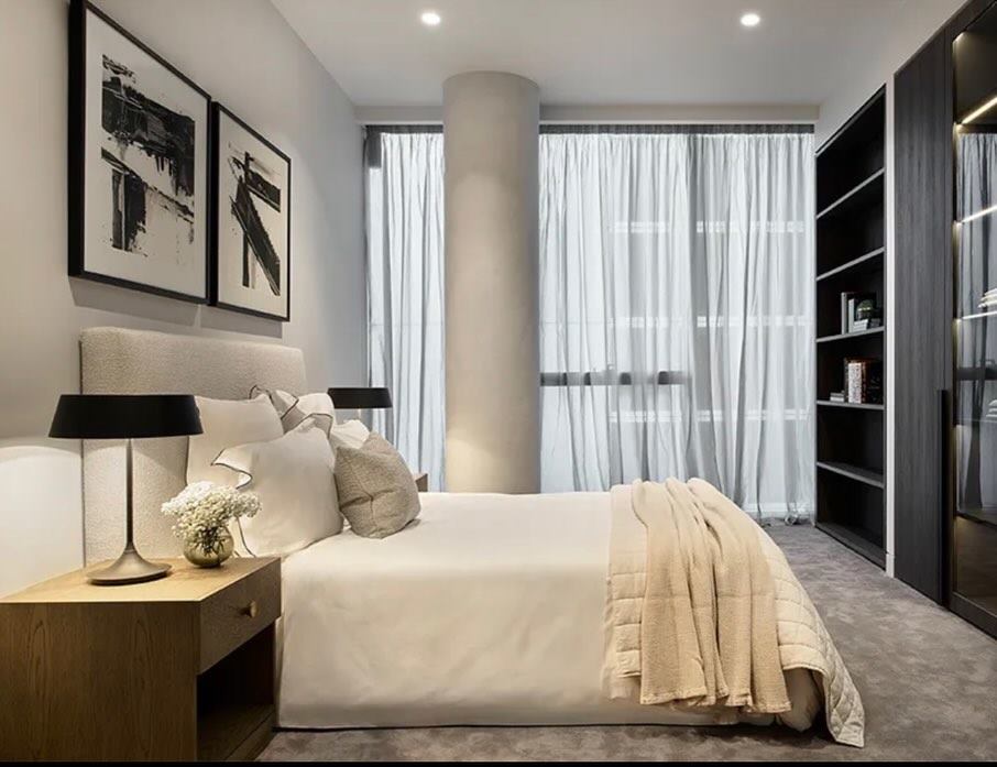 Bedroom with a rendered column, framed artwork, drapes and open shelving.