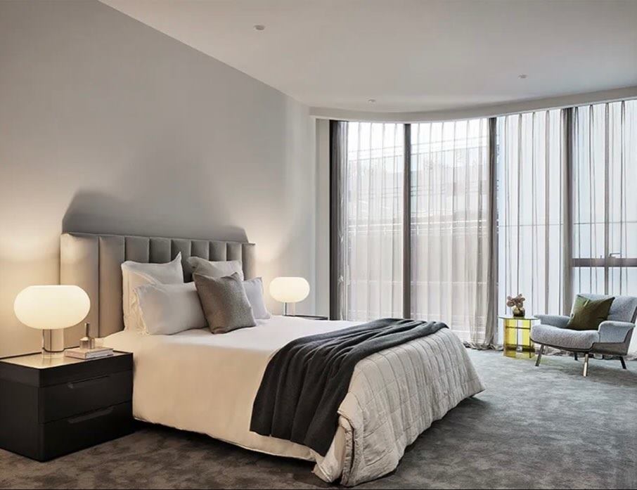 Bedroom with an upholstered bedhead, floor-to-ceiling drapes, bedside lamps and carpet.