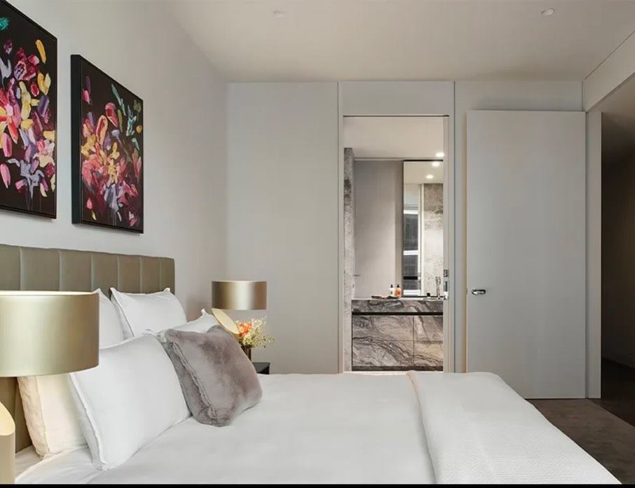 Bedroom with gold table lamps, floral artwork and a doorway through to a marble ensuite.