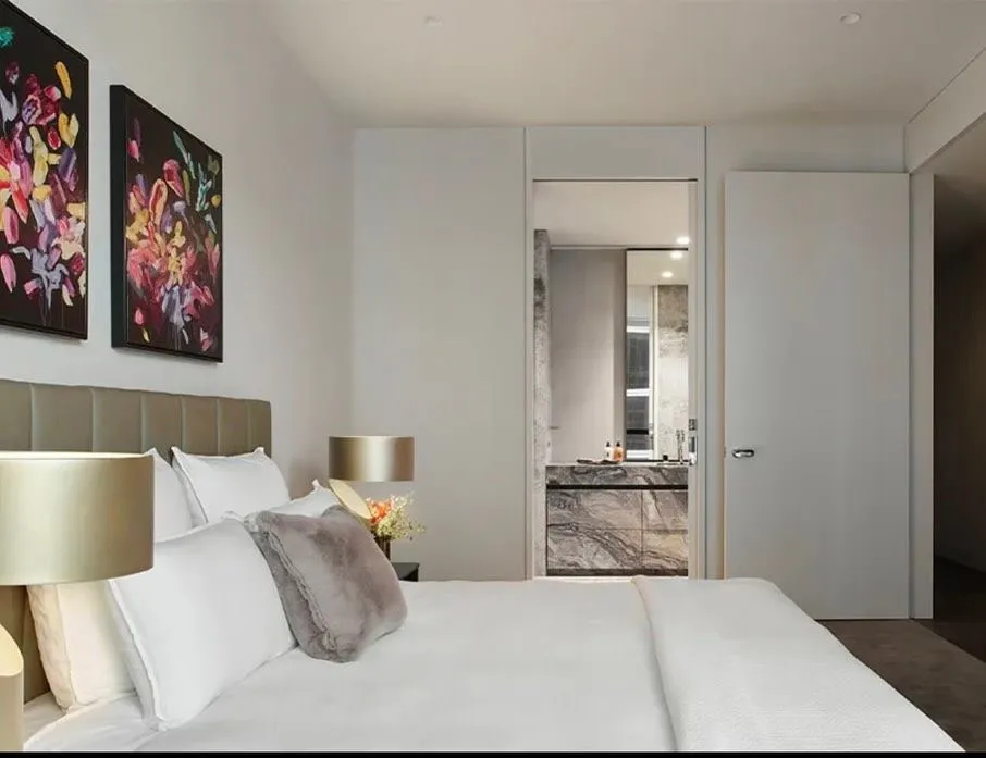 Bedroom with gold table lamps, floral artwork and a doorway through to a marble ensuite.