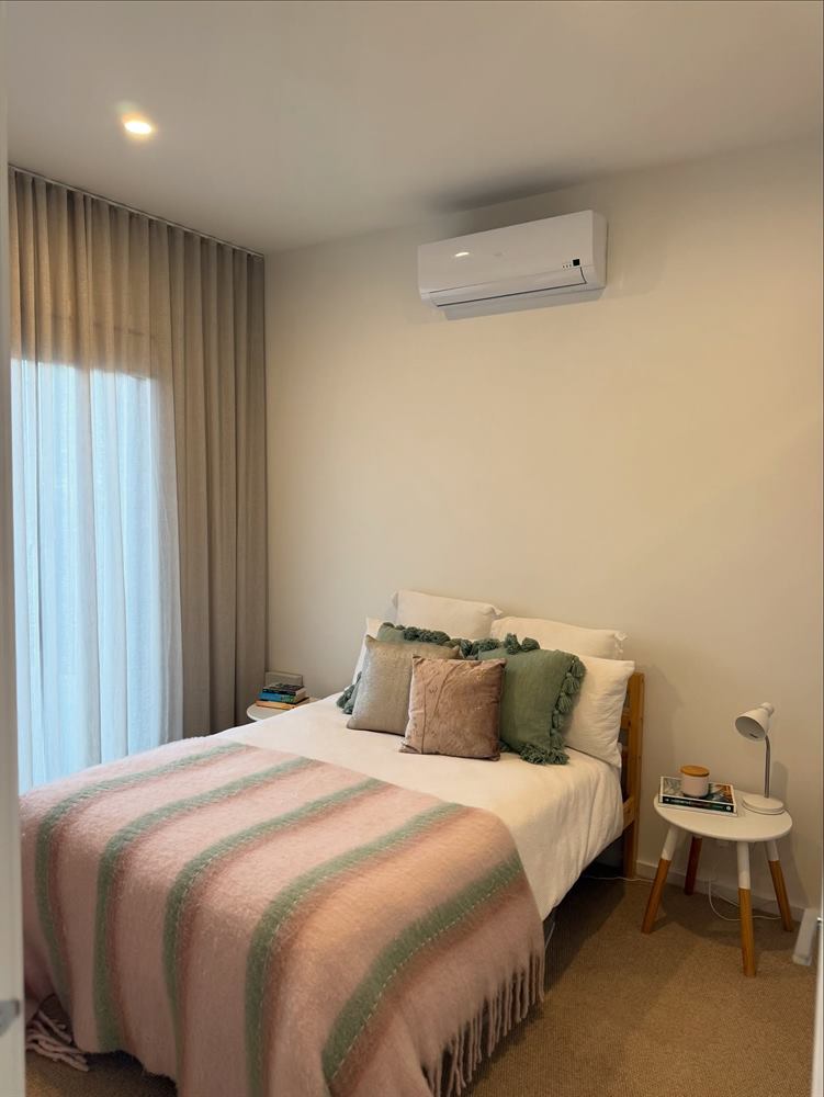 Bedroom with a striped bedspread, full-length curtains and a wall-mounted air conditioner.