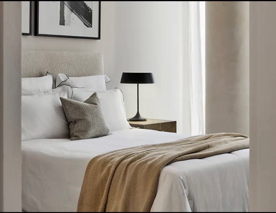 Bedroom in cream and taupe with black table lamps, framed art and full-height drapes.