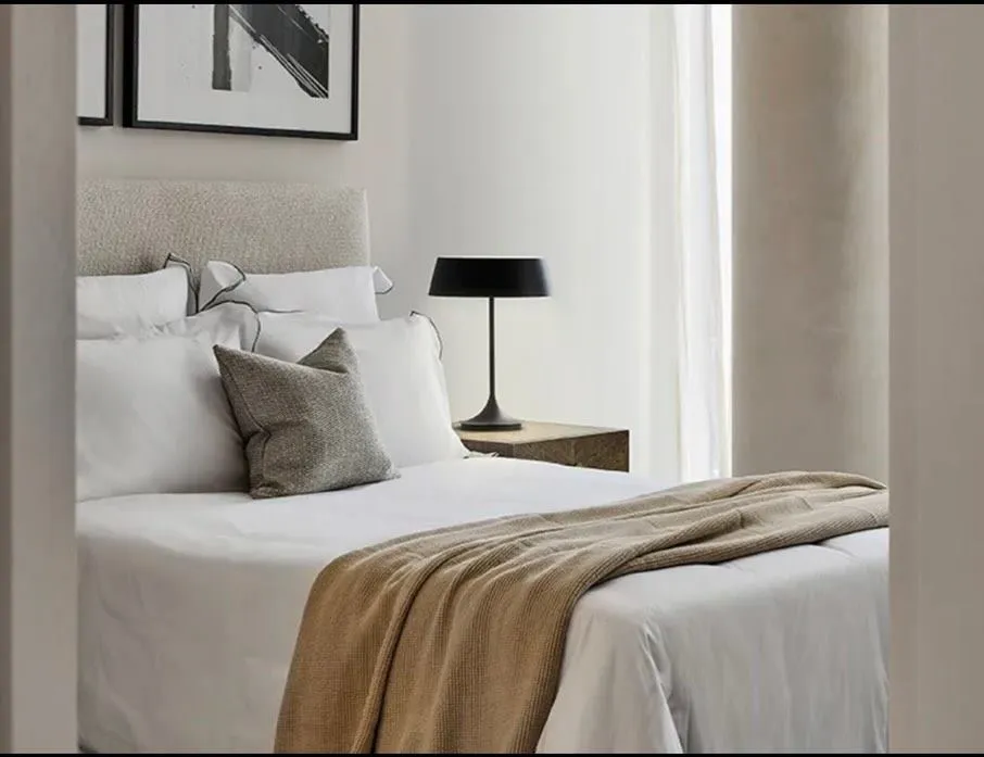 Bedroom in cream and taupe with black table lamps, framed art and full-height drapes.