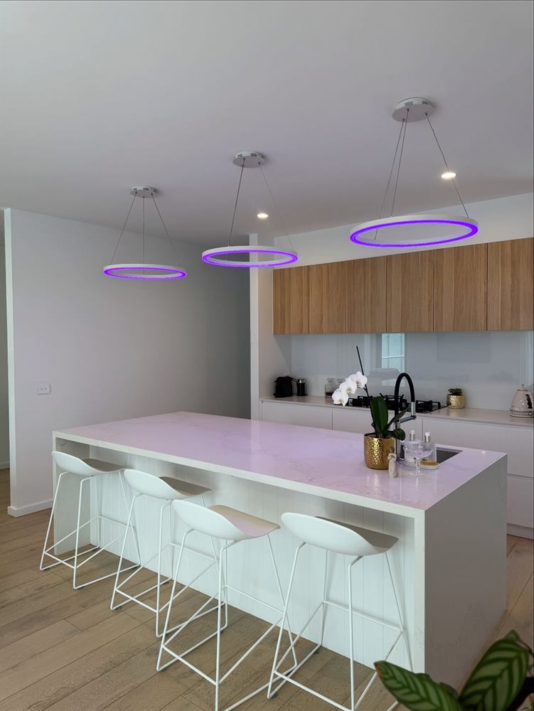 Kitchen with a white island bench, bar stools, timber joinery and violet ring pendant lights.