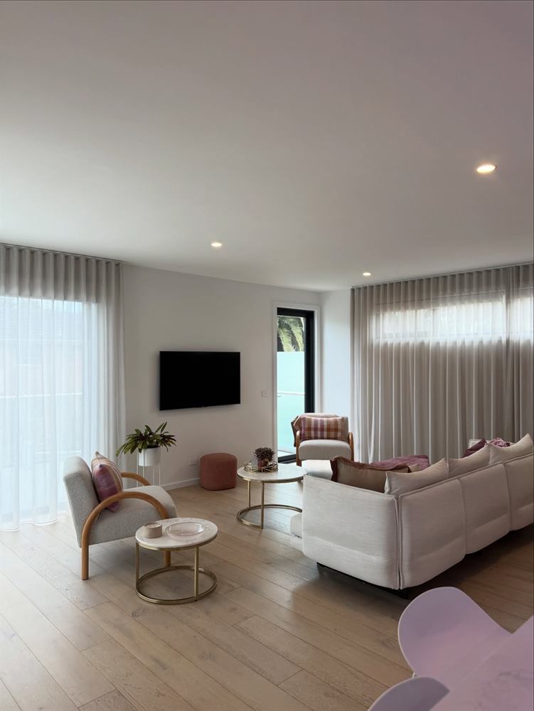 Living room with pale sofas, round coffee tables, sheer curtains and light timber floors.