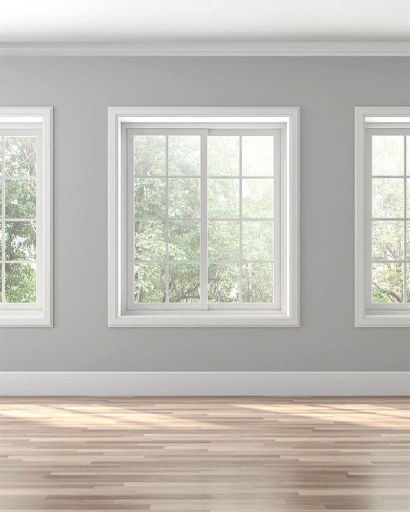 Empty room with white sash windows, panelled wainscoting and pale grey walls over timber floors.