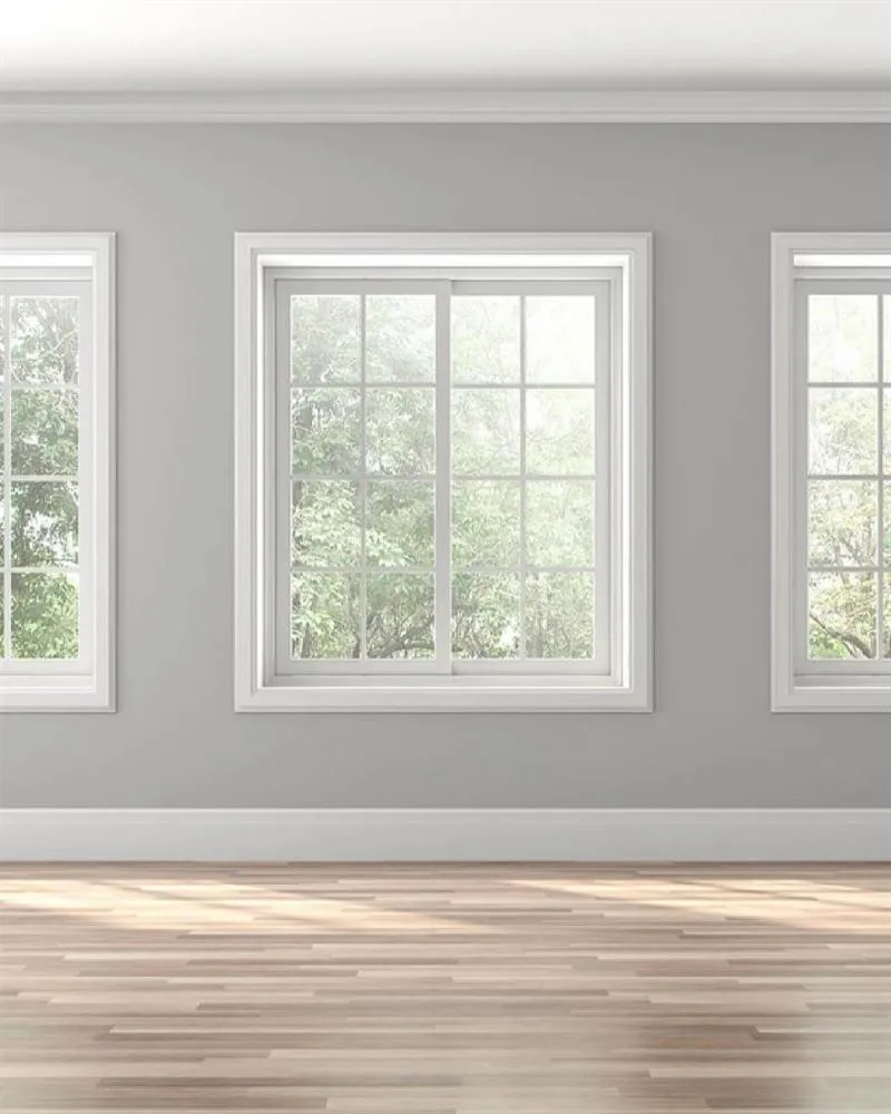 Empty room with white sash windows, panelled wainscoting and pale grey walls over timber floors.
