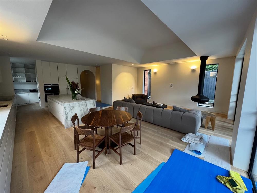 Open living and dining space with a raked ceiling, timber floors and a freestanding fireplace flue.