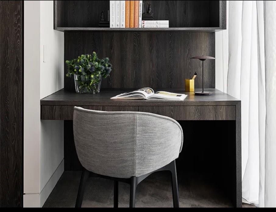 Study nook with a dark timber desk, shelving and an upholstered chair.