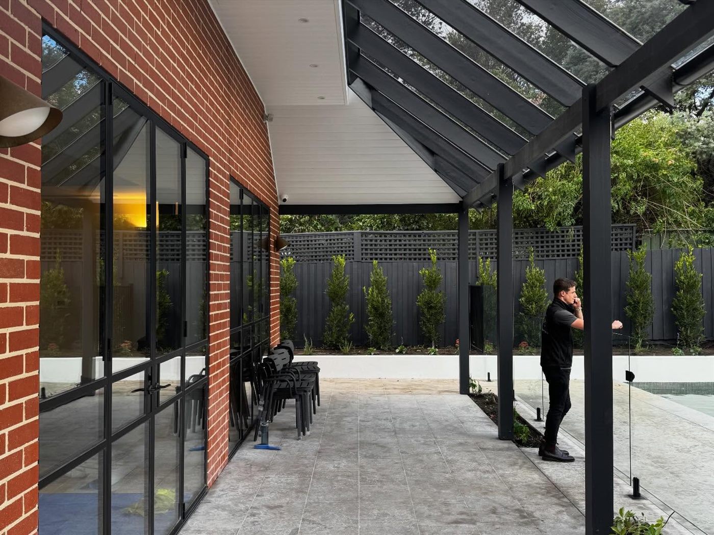 Brick courtyard beneath a black steel-framed glazed pavilion and pergola.