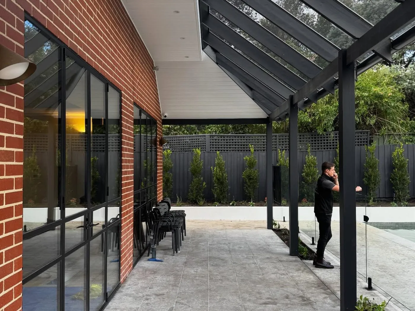 Brick courtyard beneath a black steel-framed glazed pavilion and pergola.