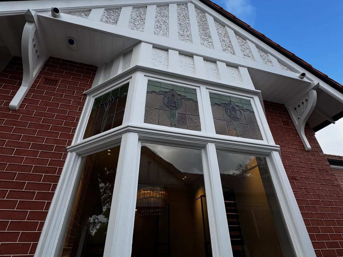 Red-brick bay window with white timber fretwork and leadlight glazing, seen from below after repainting.