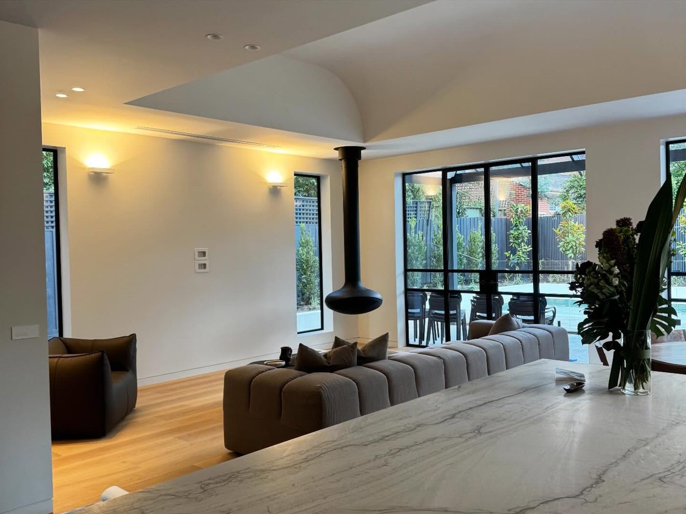 Open living and dining space with a curved bulkhead ceiling, marble floor and black steel-framed windows.