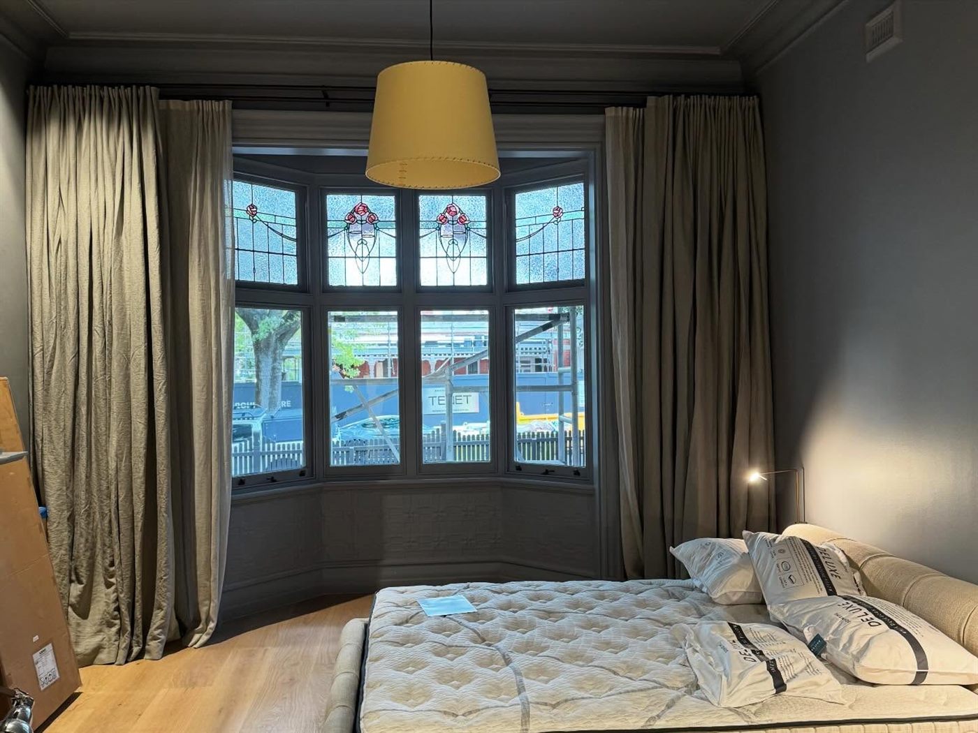 Bedroom with a leadlight bay window, heavy curtains and a drum pendant light.