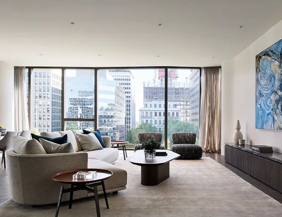 Apartment living room with floor-to-ceiling glazing onto a city skyline, pale sofas and artwork.