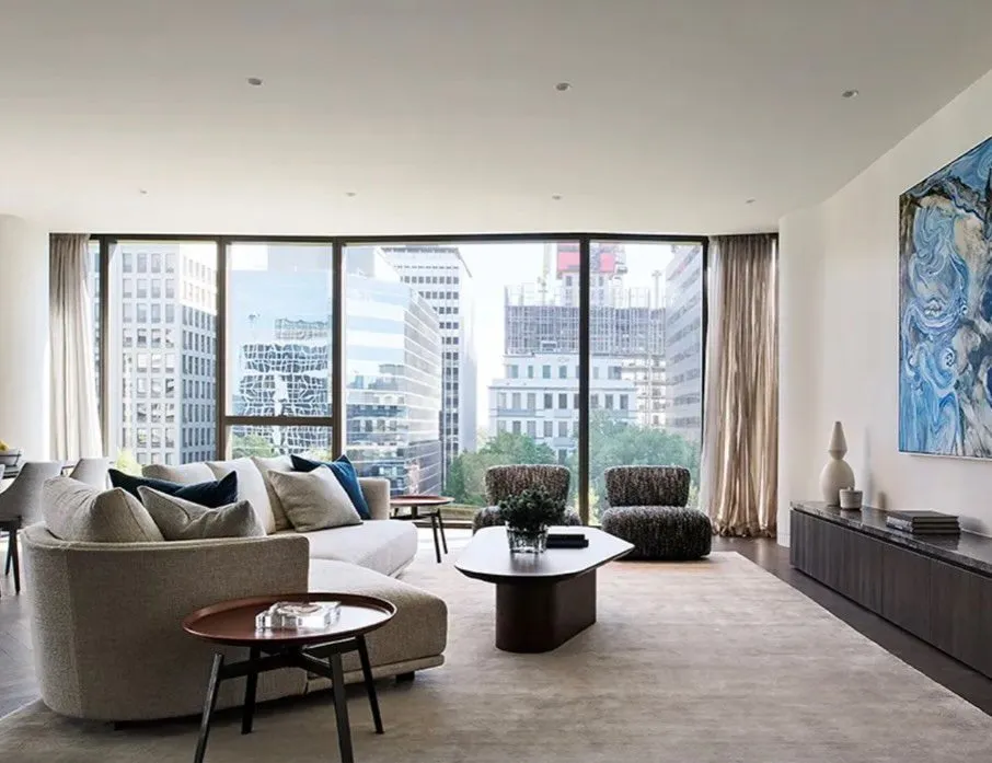 Apartment living room with floor-to-ceiling glazing onto a city skyline, pale sofas and artwork.