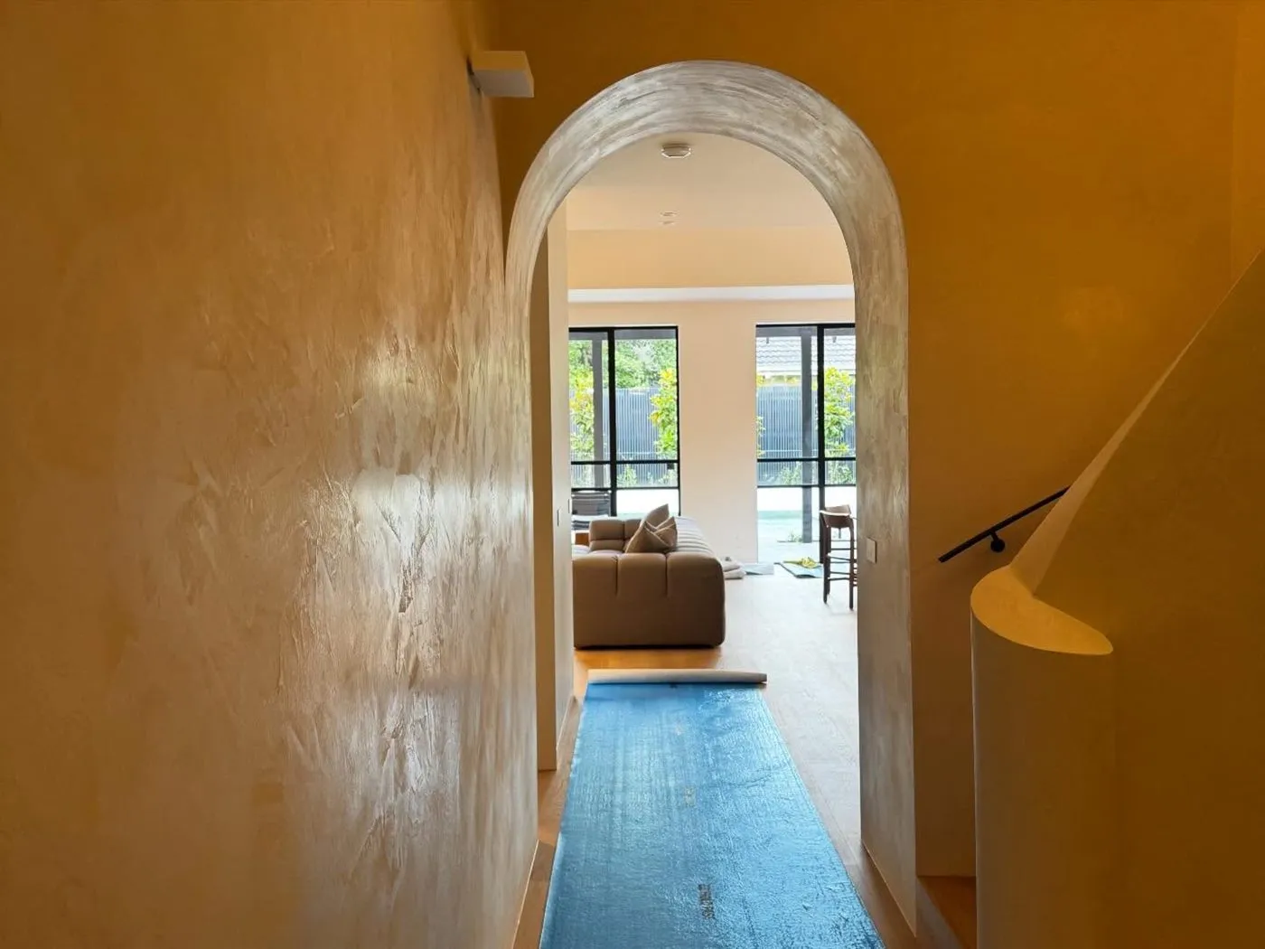 Ochre limewashed hallway with a rendered arch opening onto a living room.