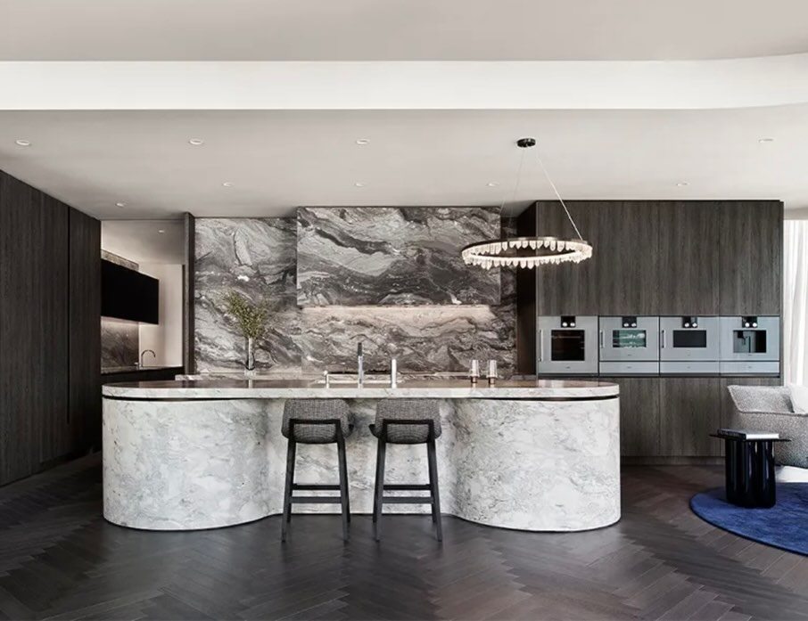 Kitchen with a curved veined-stone island, dark timber joinery and a circular pendant light.