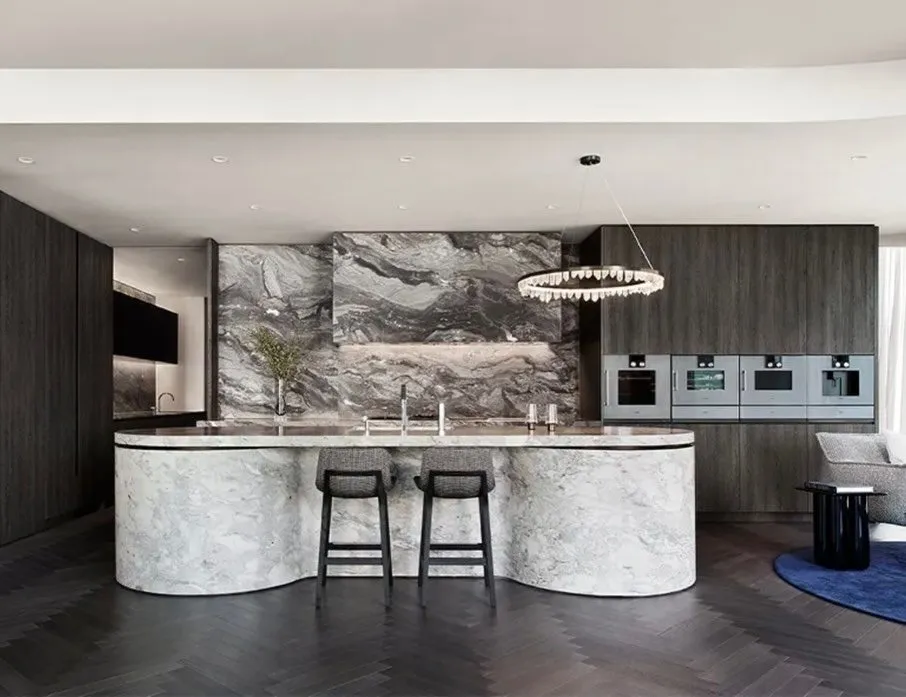 Kitchen with a curved veined-stone island, dark timber joinery and a circular pendant light.
