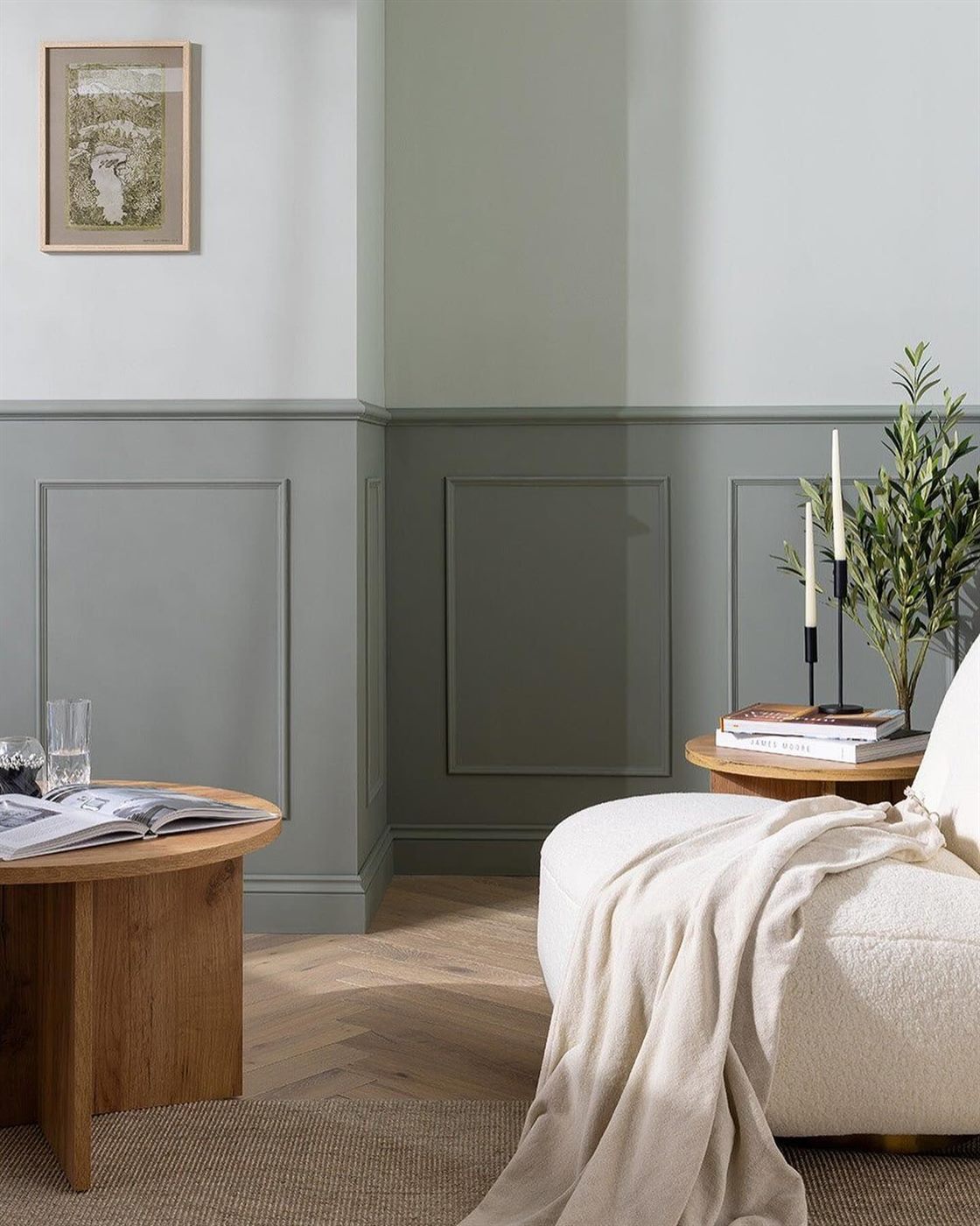 Bedroom with sage-green panelled wainscoting, framed artwork and an oak side table.