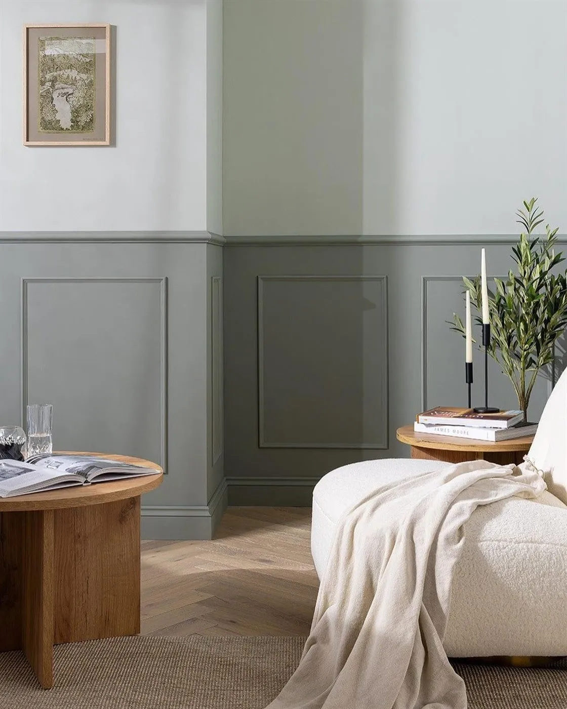 Bedroom with sage-green panelled wainscoting, framed artwork and an oak side table.