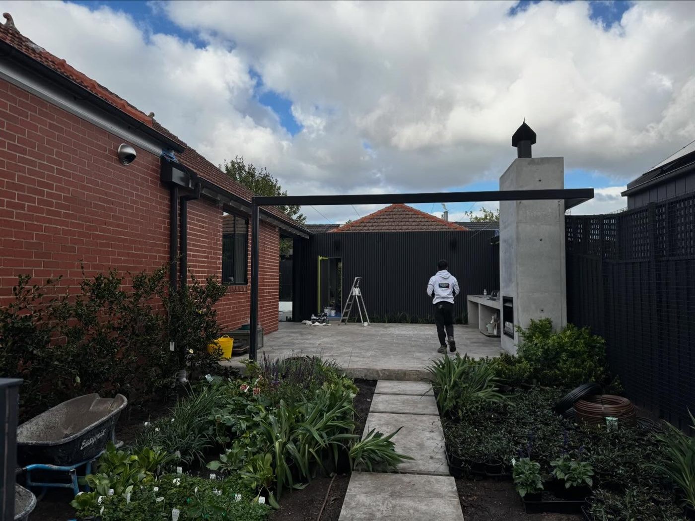 Brick side path and garden beds beside a rendered wall and dark boundary fence.