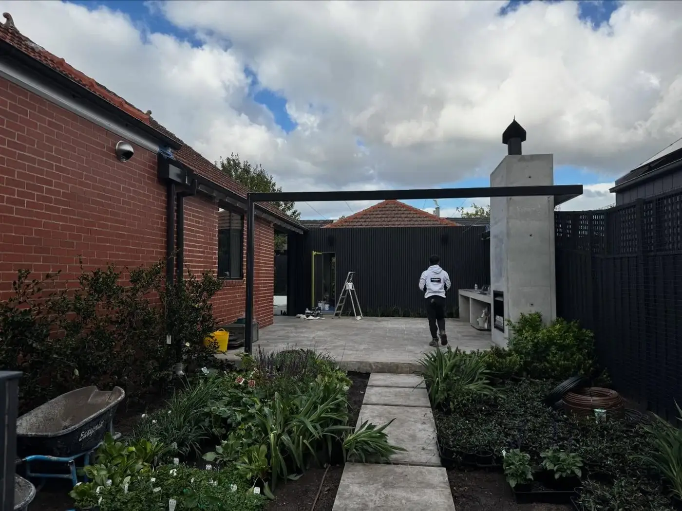 Brick side path and garden beds beside a rendered wall and dark boundary fence.