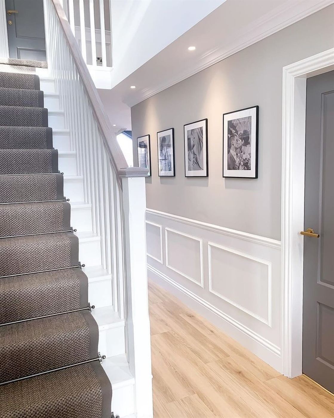 Staircase with white panelled wainscoting, grey walls, framed prints and a grey runner.